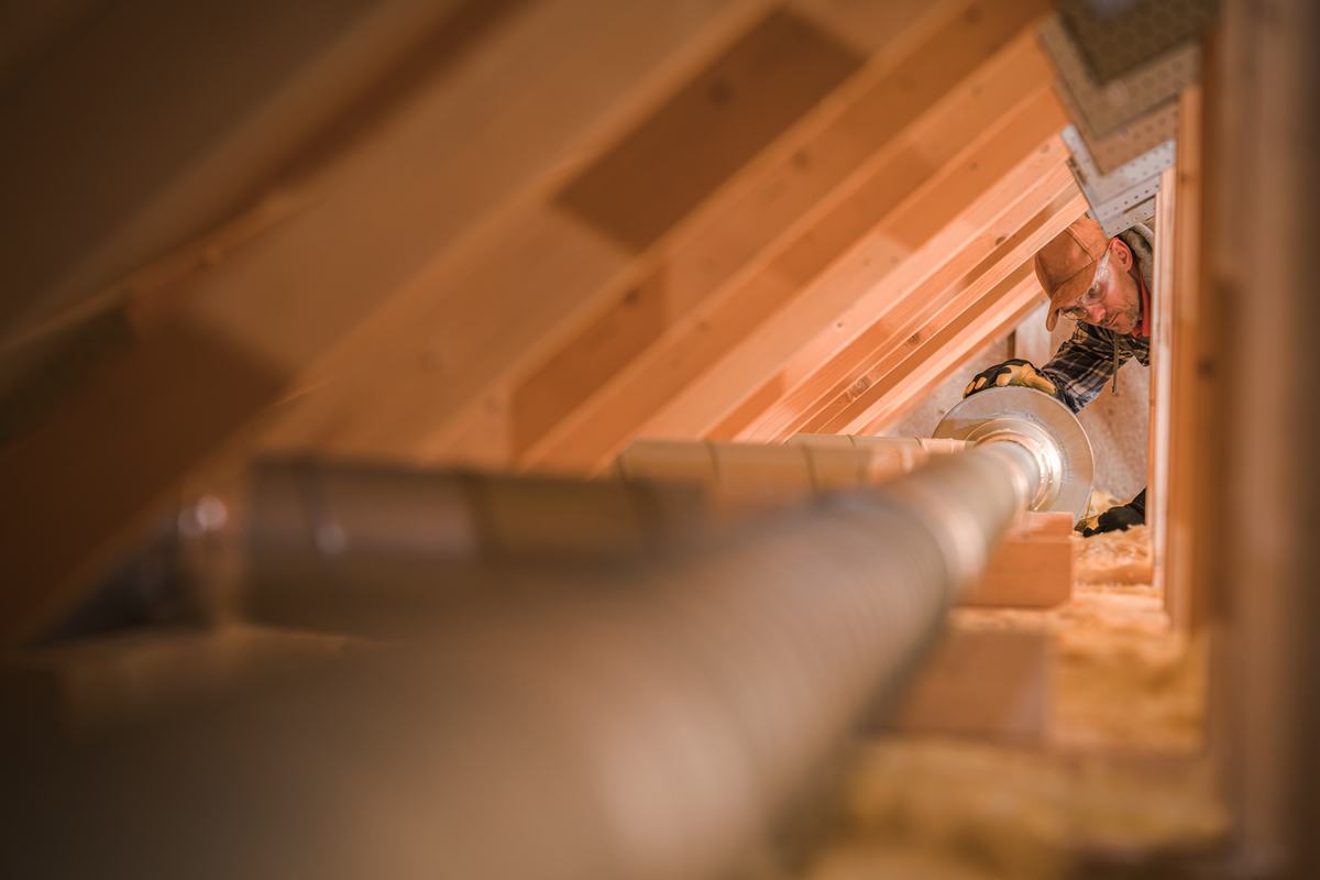An HVAC technician working on insulated ductwork in an attic
